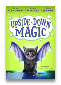 Book cover of a gray cat with purple and blue bat wings coming out of its sides on a green background. Above the cat is a white cloud with the words Upside-Down Magic. 
