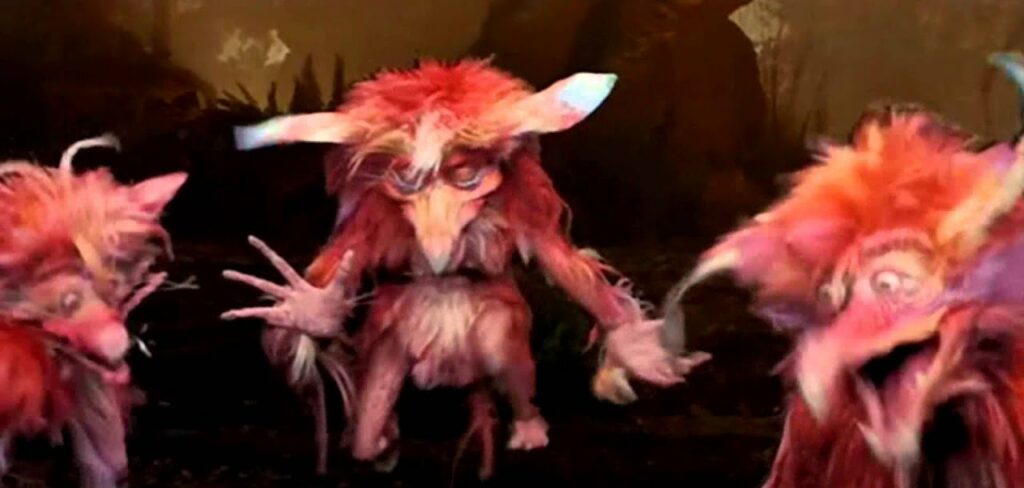 film still from Labyrinth depicting red furry creatures, the Fireys, dancing in a dark forest