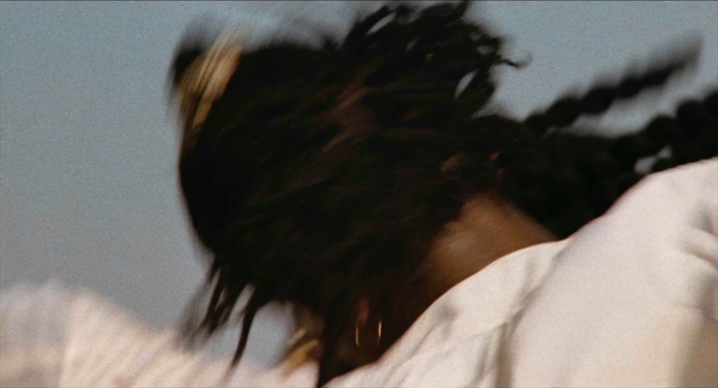 film still depicting the blurry head and shoulders of a woman dancing in a white dress