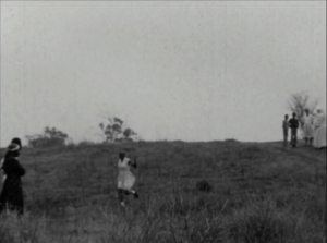 black and white film still depicting a girl run down a grassy hill away from a group of children and nuns toward her mother and father