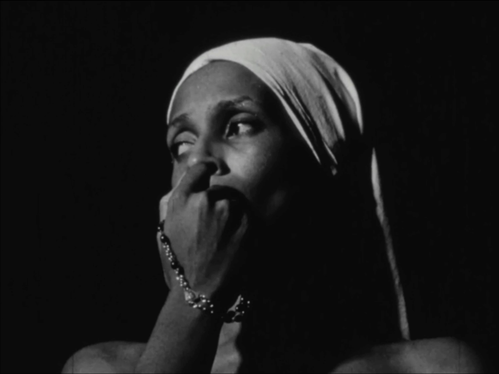 black and white film still depicting a woman with covered hair holding a rosary to her face as she looks to the left