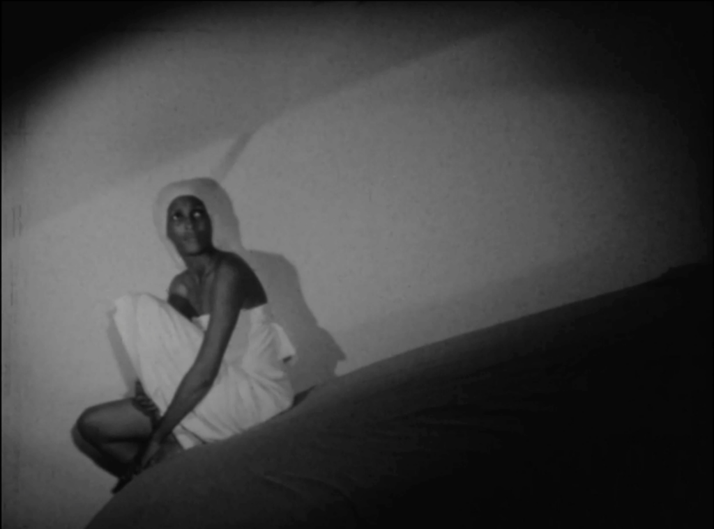 black and white film still depicting a woman sitting at the edge of her bed, camera tilted so she appears askew