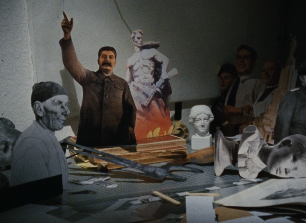 film still depicting an artist's studio strewn with cut-out standees on top of and around a large worktable