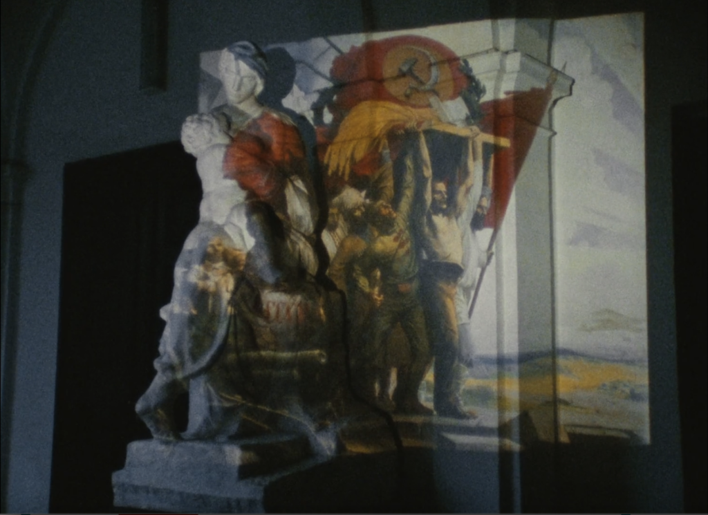film still depicting a Socialist Realism style painting being projected onto a classical-style sculpture 