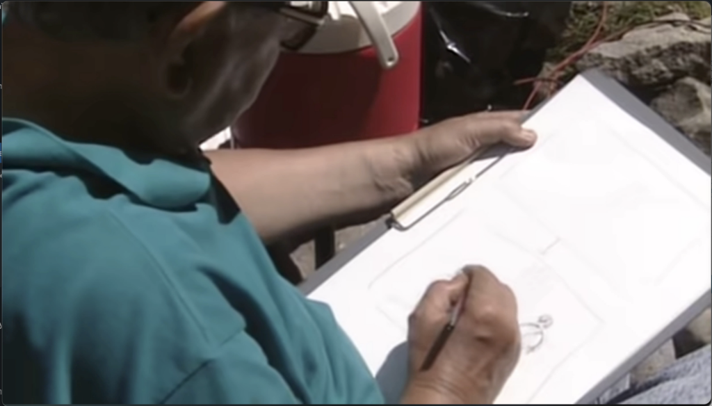 over the shoulder photograph of man in teal polo bent over a clipboard and drawing