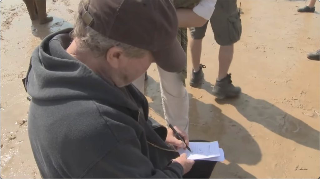 over the shoulder photograph of a man sitting, bent over and drawing on loose paper