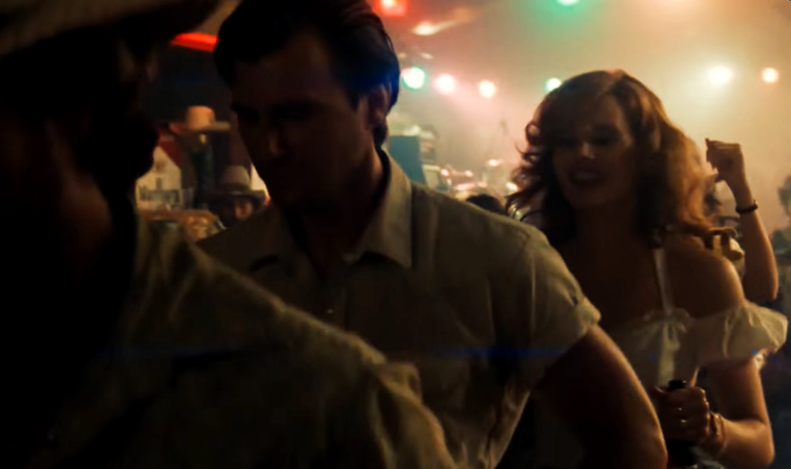 film still from Thelma & Louise depicting two line-dancing men silhouetted left of frame while woman dances behind them, surrounded by hazy multicolor lights