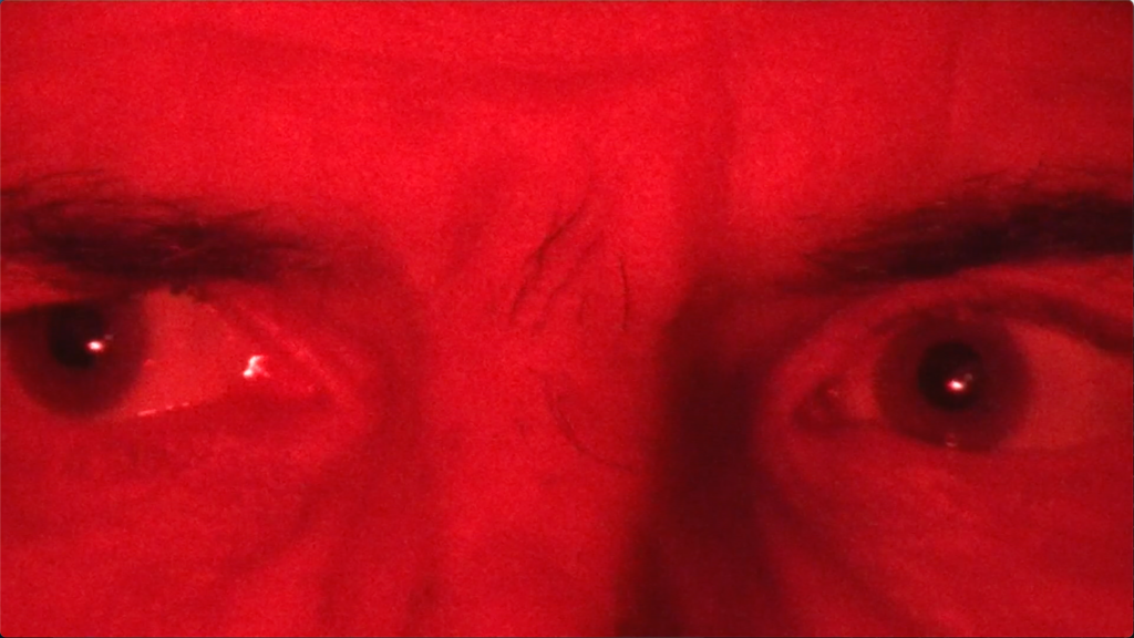 film still depicting extreme close up of a man's eyes flooded in red light while he looks off screen