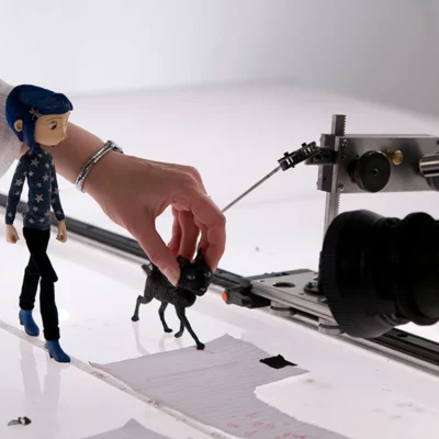 a hand repositions a claymation cat and young girl, which are held up with wires in a white space