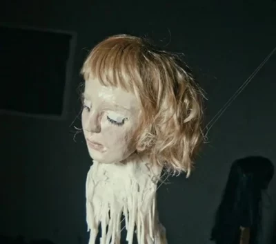 film still depicting papier-mâché head of a woman with strips of masking tape hanging from her neck