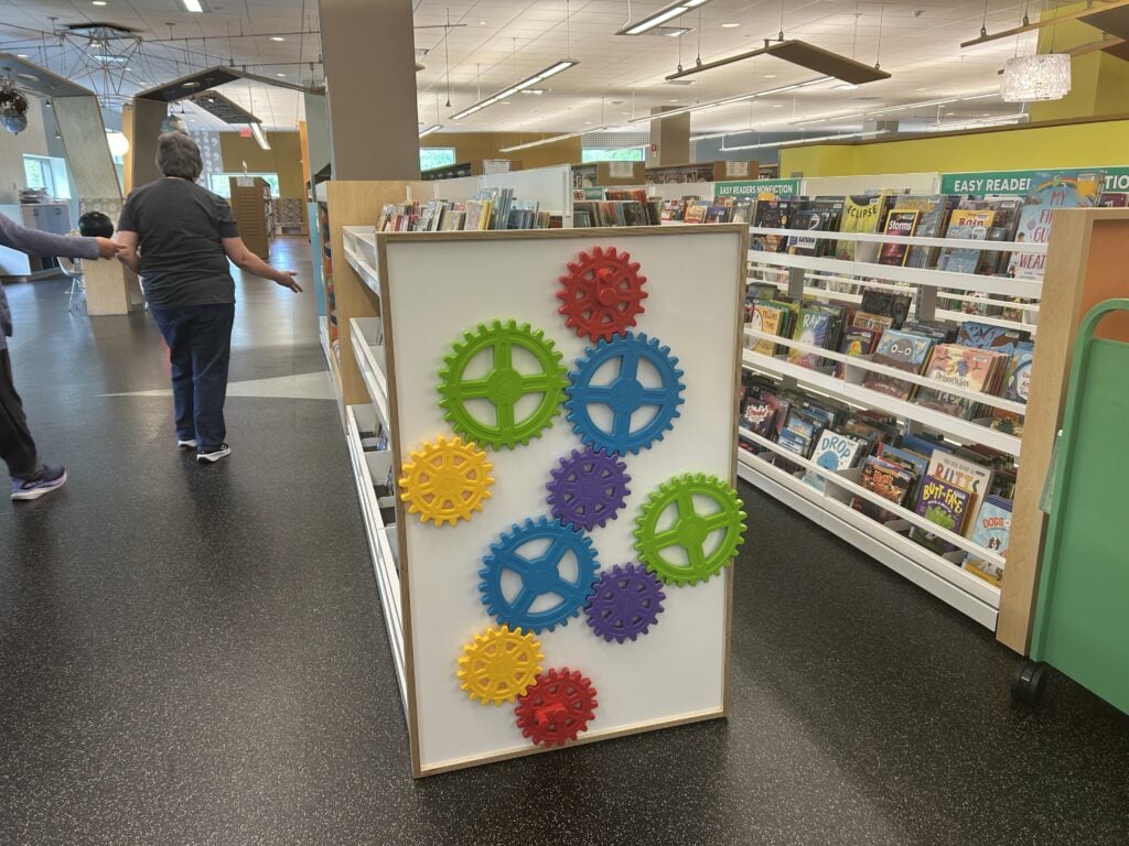 A library display shelf with colorful interlocking gears mounted on the end.