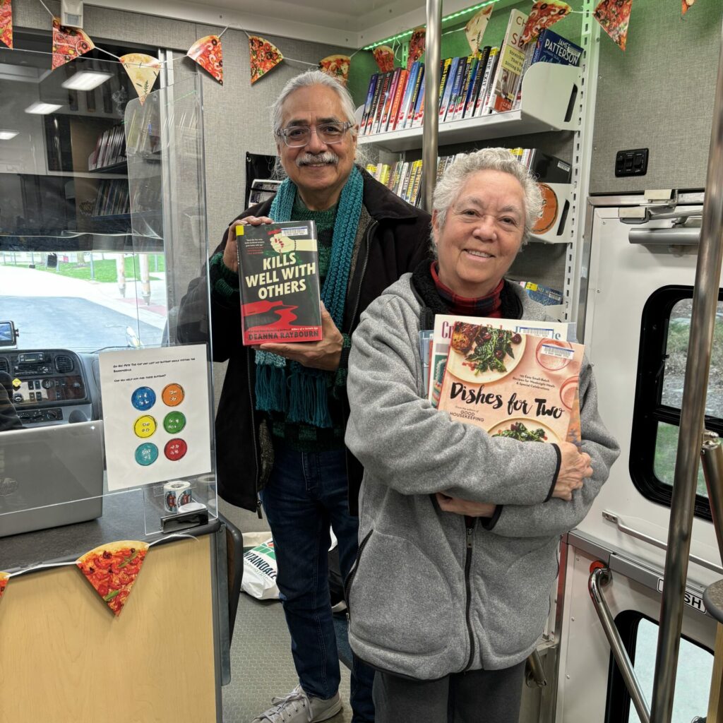 Library patrons standing inside the Bookmobile, smiling and holding books.