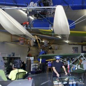 A small aviation museum with vintage aircraft suspended from the ceiling and a person in a helmet standing beside a display case.