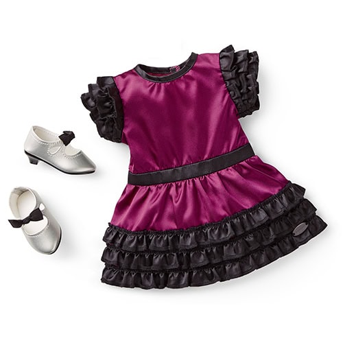 A purple and black ruffled dress with short sleeves is displayed next to a pair of silver dress shoes with bows.