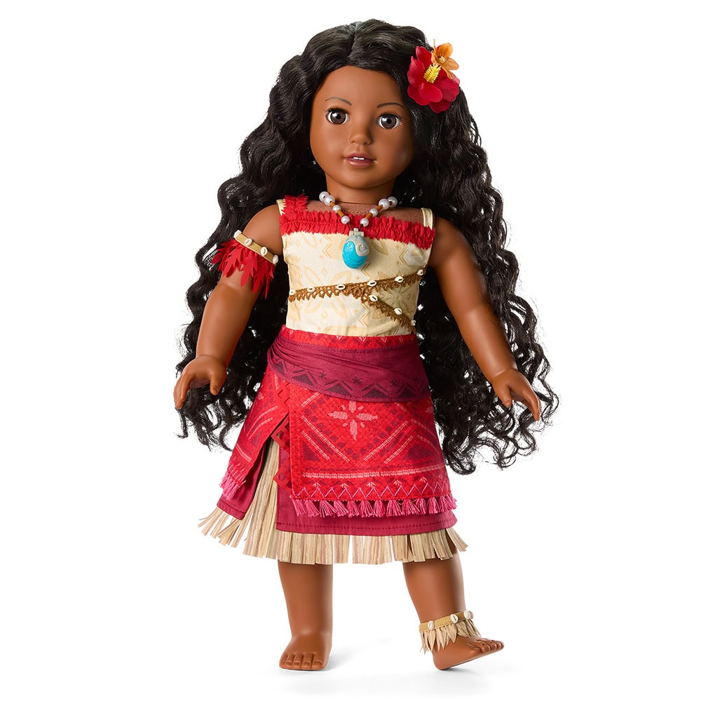 A doll with long curly black hair, a flower in her hair, a patterned red and tan dress, a blue pendant necklace, and barefoot with an anklet.