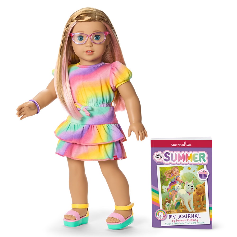 A blonde doll in glasses wearing a rainbow dress and sandals stands next to a “Summer” journal book with a dog and girl on the cover.