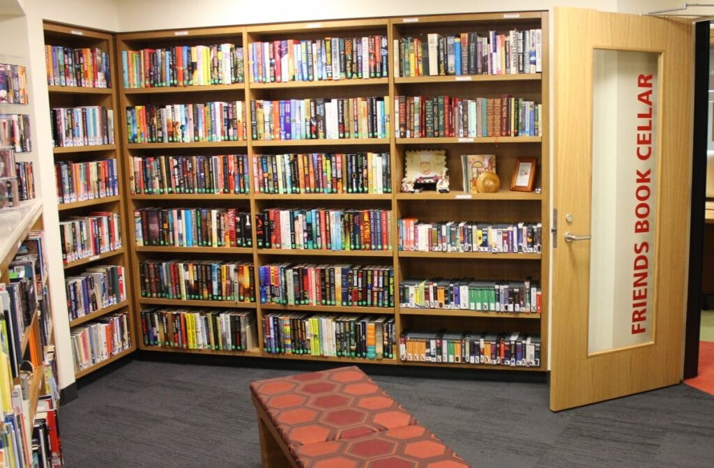 Bookshelves filled with a variety of books, a glass door labeled "Friends Book Cellar," and a cushioned bench in the foreground.