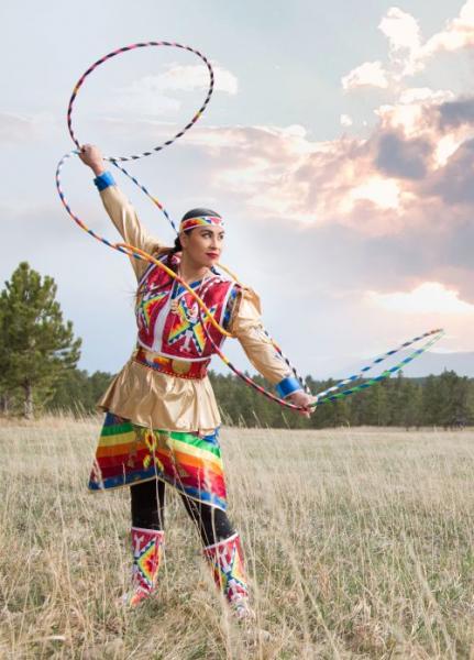 Starr Chief Eagle in colorful traditional regalia performs a hoop dance in a grassy field