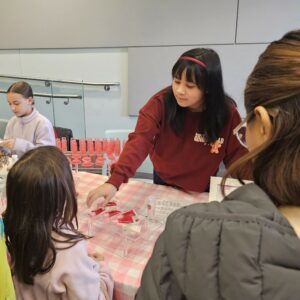 A girl in a red sweatshirt explains items on a table to a child