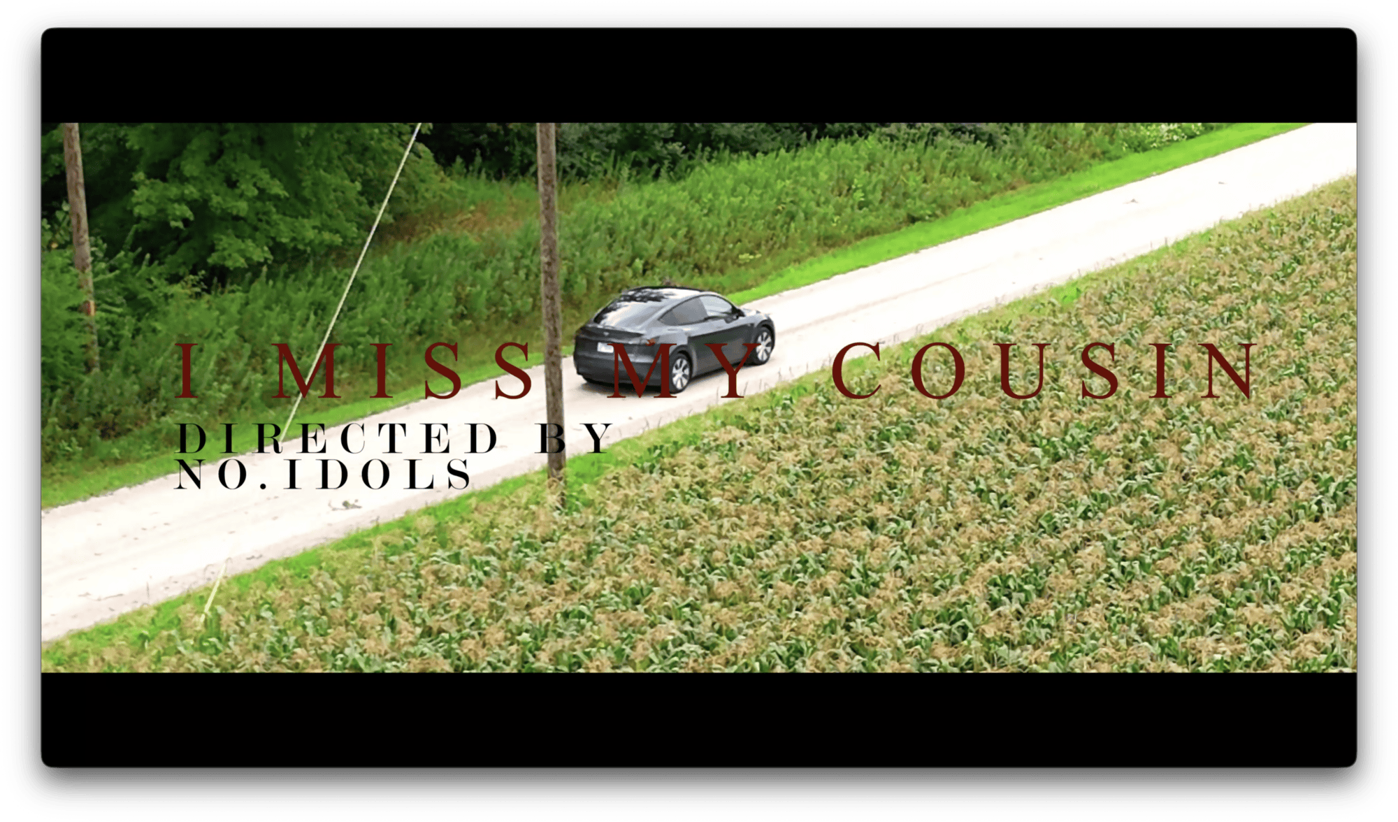A black car drives on a rural road next to a field. Overlaid text reads:
