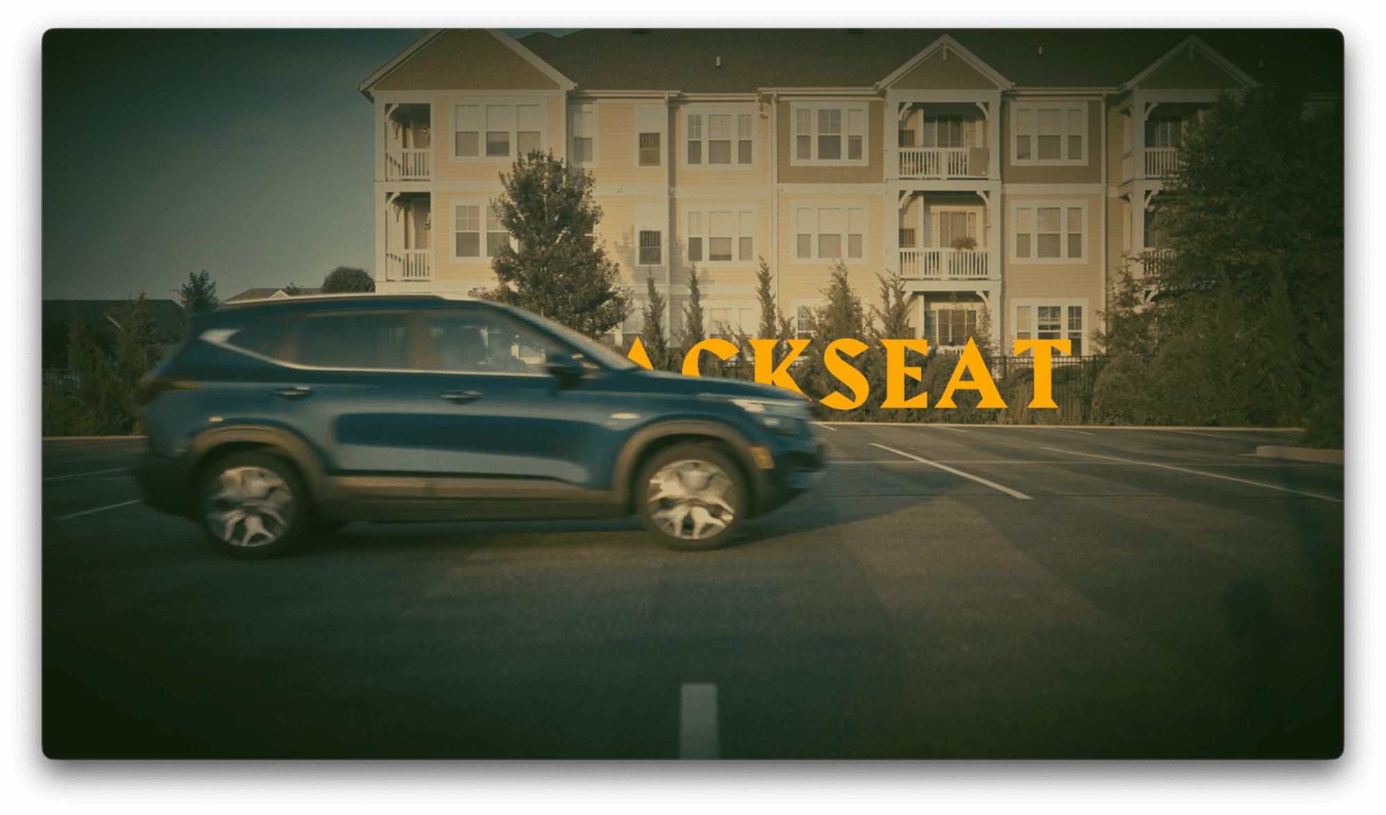 A blue SUV drives through an empty parking lot in front of an apartment building; the word