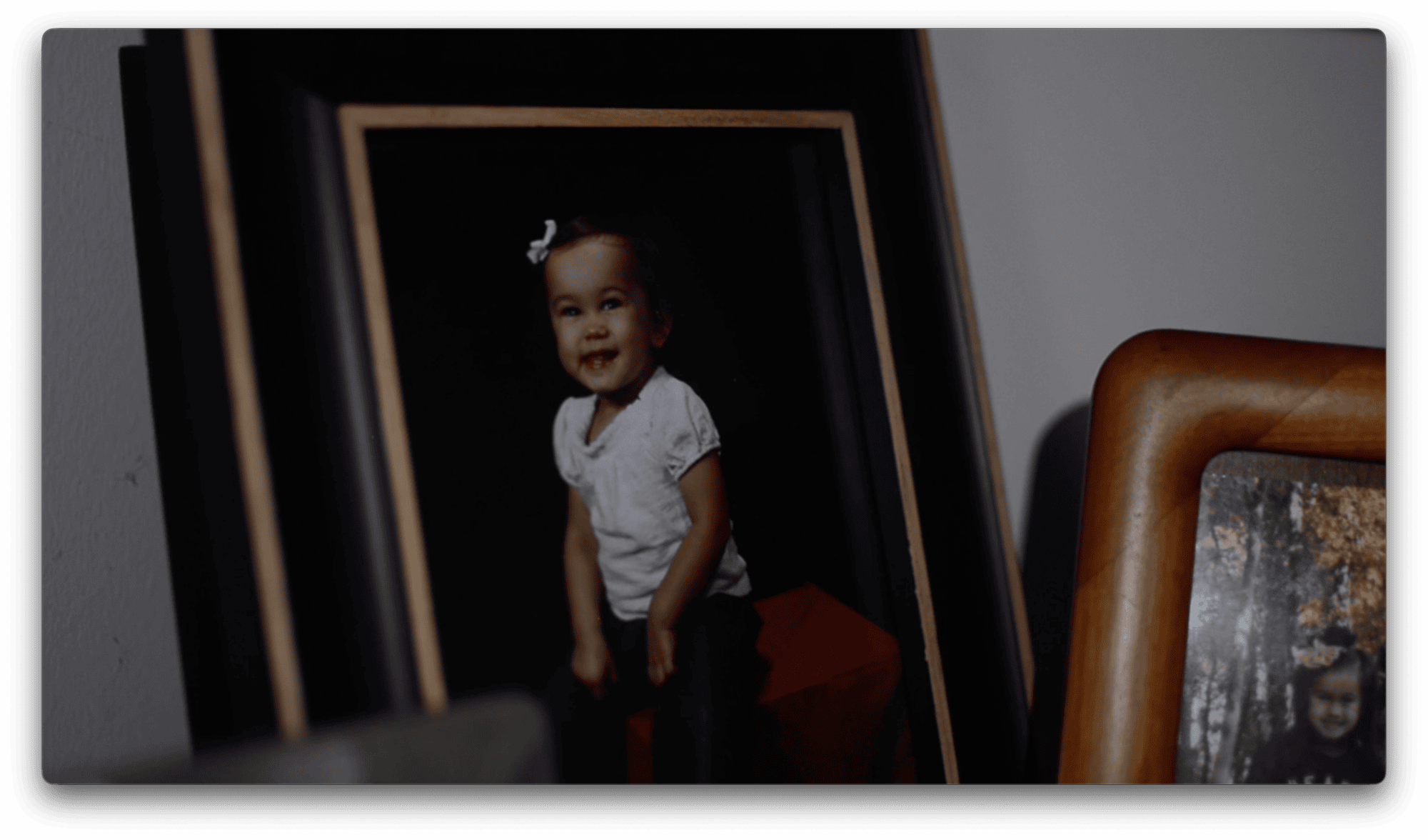 Framed photograph of a smiling toddler with a white bow in her hair, next to another partially visible framed photo.