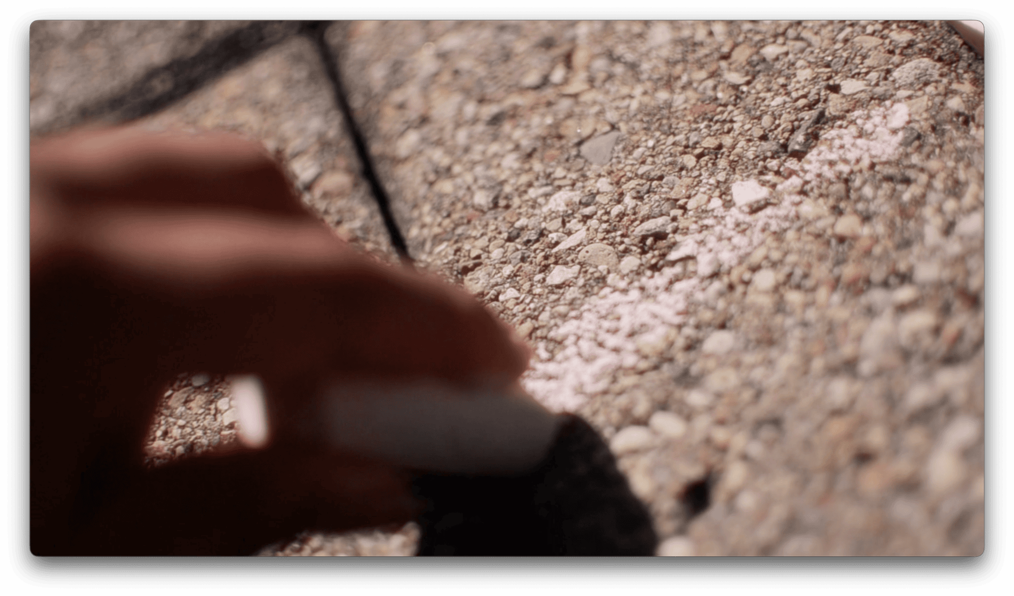 A hand draws a pink chalk line on rough concrete pavement.