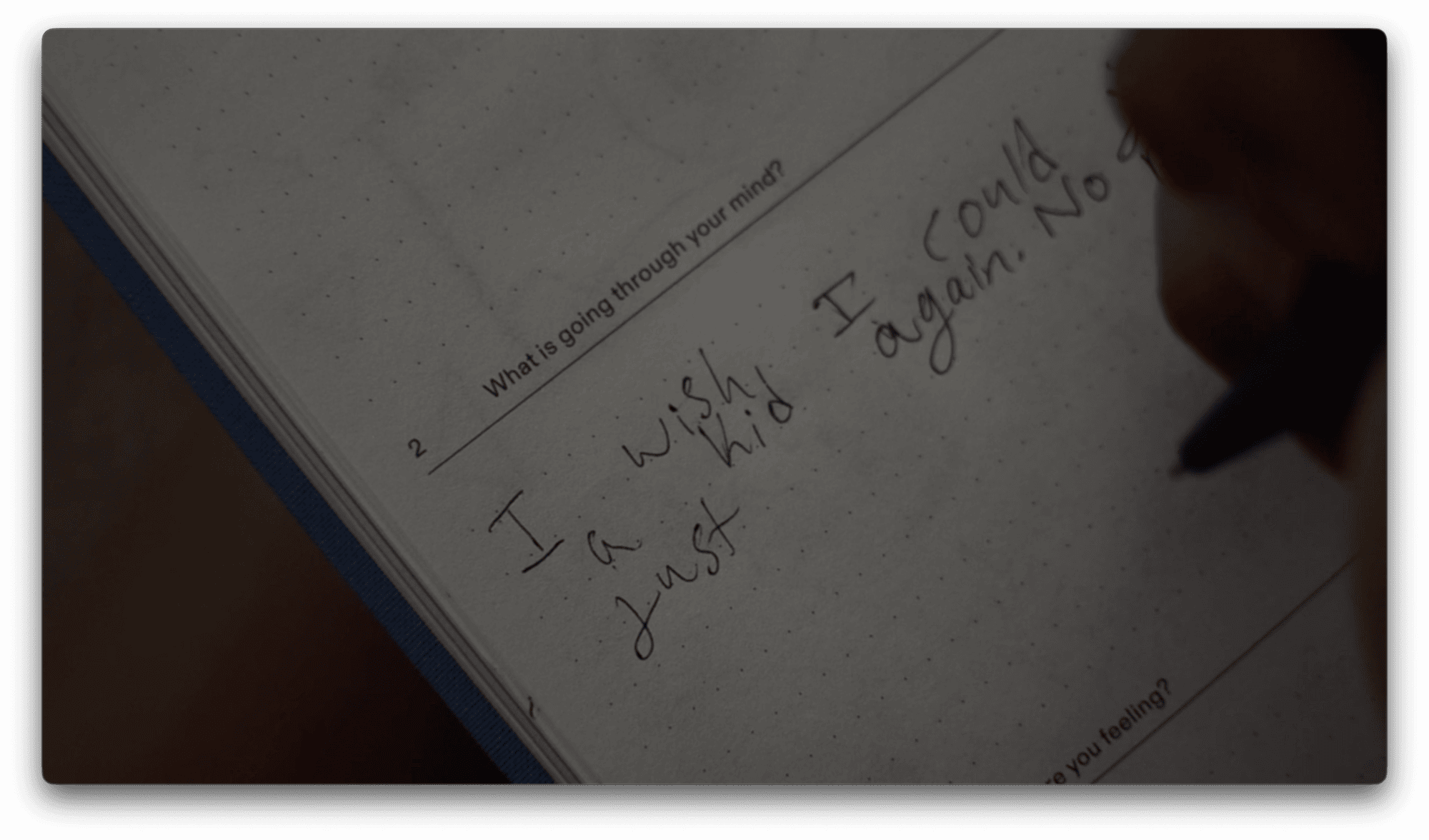 A hand writes in a journal on a dotted page under the prompt