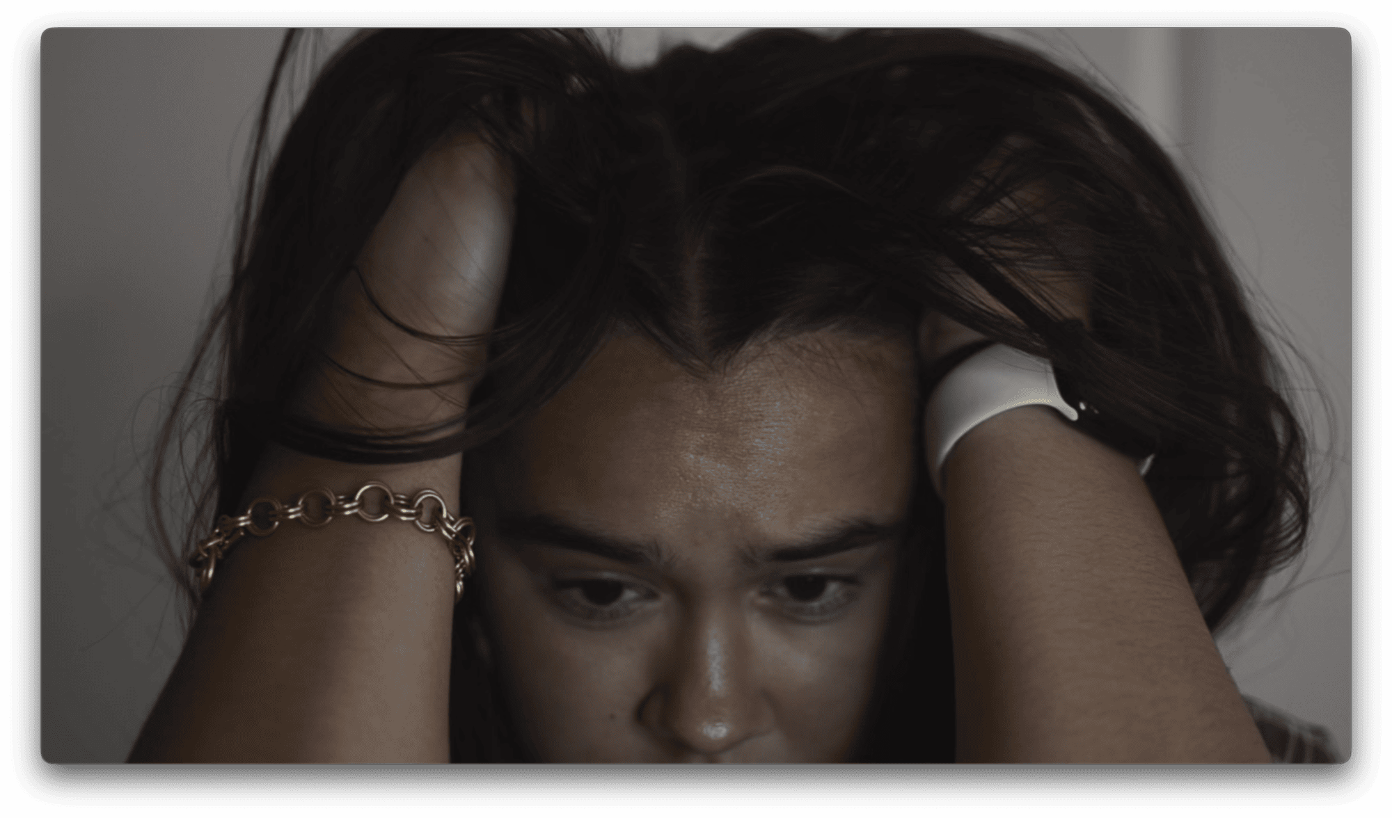 A person holding their head with both hands, looking down with a distressed expression.