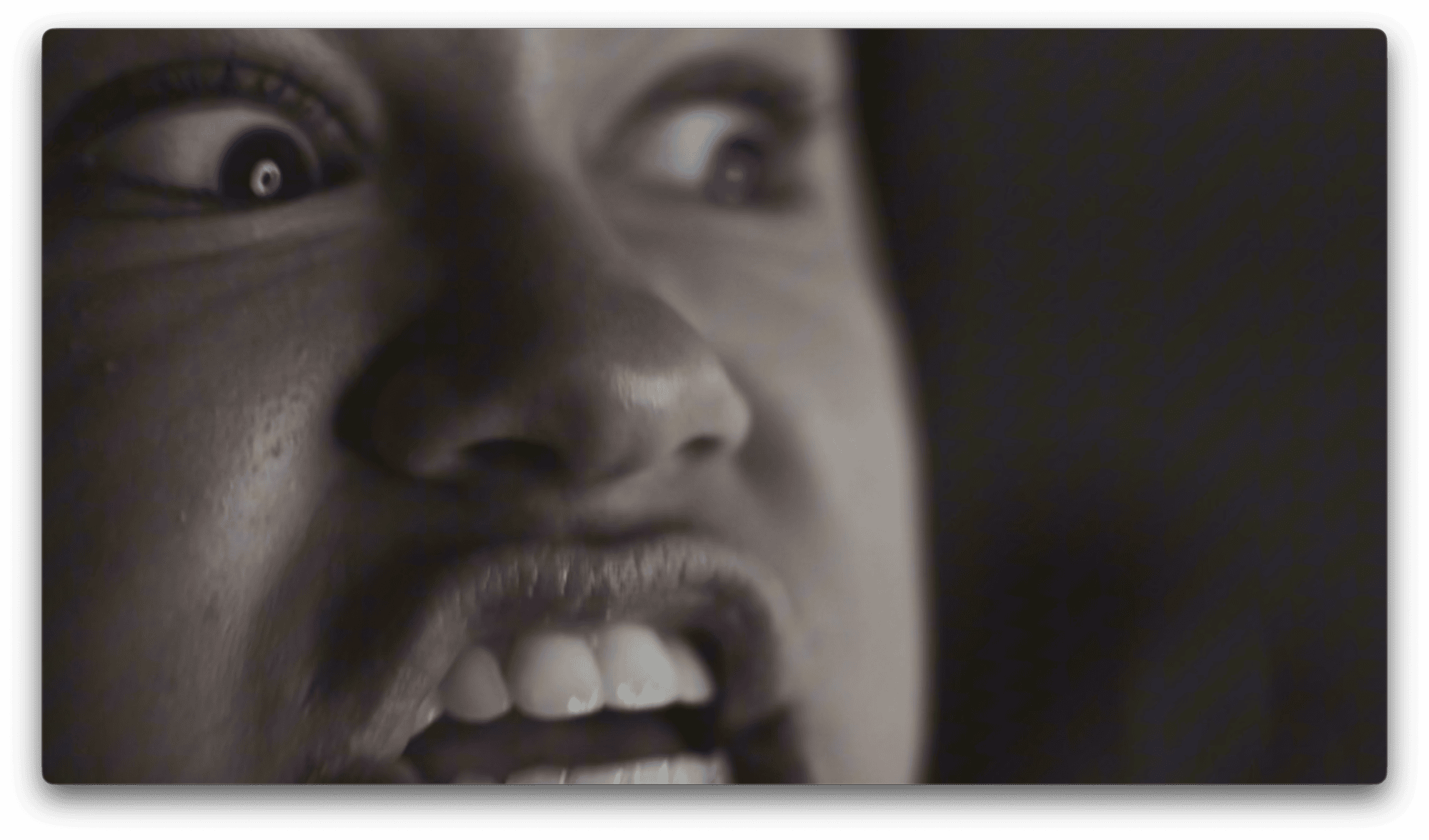 Close-up of a person's face showing wide eyes and a tense, open mouth, appearing to express anger.