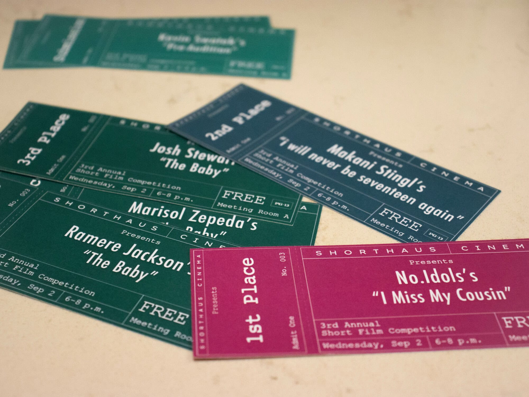 Five colorful award tickets for a short film competition are arranged on a light surface, displaying placements from first to third place and film titles.